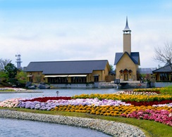 なばなの里の風景。手入れされた花畑と池の向こうに、塔のある建物がある